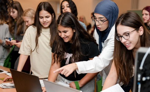 Gruppe junger Frauen, die gemeinsam an Laptops arbeiten und diskutieren.