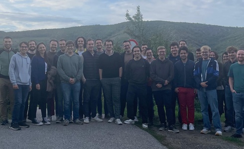 Eine Gruppe von etwa 30 Menschen steht lächelnd im Freien vor einer Landschaft.