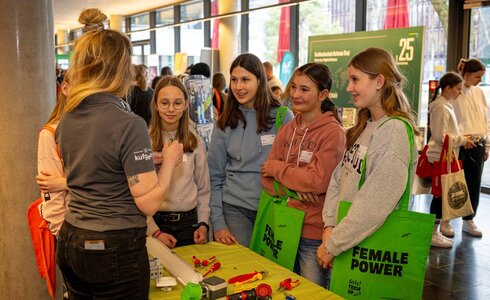 Eine Gruppe von Mädchen hört einer Frau am Infostand aufmerksam zu.