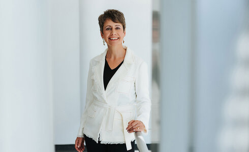 Eine lächelnde Frau in einer weißen Jacke steht an einem Geländer.