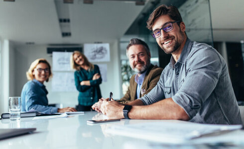 Vier Personen in einem Besprechungsraum, lächeln und schauen direkt in die Kamera.