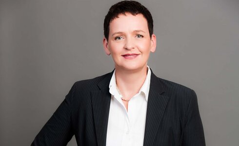 Porträt einer Frau in Businesskleidung mit kurzer Frisur, freundlich lächelnd.