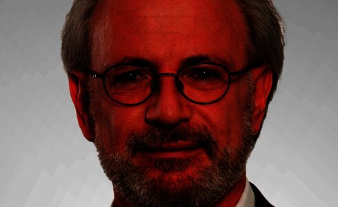 Ein älterer Mann mit Brille und grauen Haaren, lächelt freundlich in die Kamera.