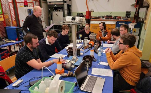 Eine Gruppe von acht Personen diskutiert an einem Tisch mit technischen Geräten.