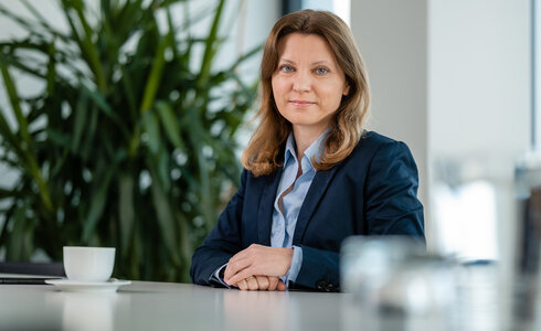Frau in einem Anzug sitzt an einem Tisch, Blick in die Kamera gerichtet.