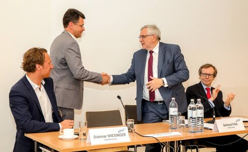 Zwei Männer schütteln sich die Hände während einer Pressekonferenz.