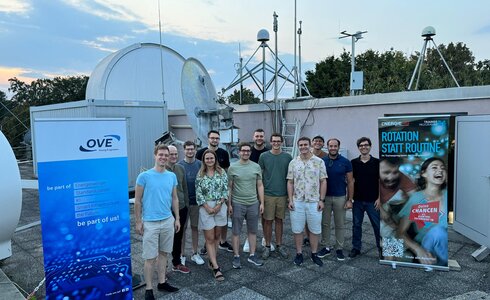 Gruppe von Personen auf einem Dach mit Werbebannern und technischen Geräten im Hintergrund.