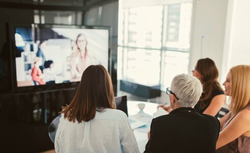 Vier Personen in einem Meeting schauen auf einen Bildschirm mit Videokonferenz.