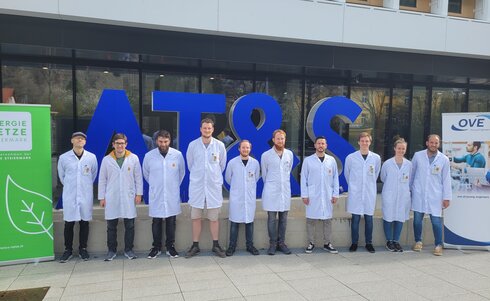 Gruppensfoto von zwölf Personen in weißen Kitteln vor einer großen blauen Schrift.