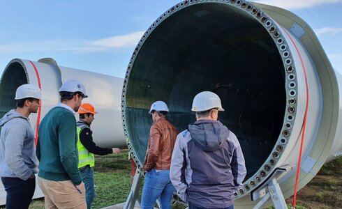 Fünf Personen in Schutzhelmen betrachten einen großen Windturbinen-Rotor.