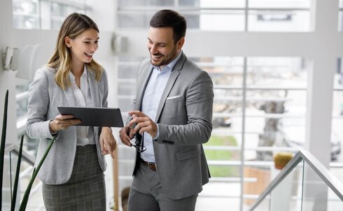 Zwei Personen in Anzügen besprechen Inhalte auf einem Tablet.
