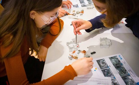 Zwei Mädchen arbeiten an einem Experiment mit Elektronikbauteilen am Tisch.