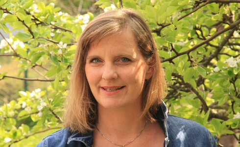 Frau mit blonden Haaren steht vor blühenden Zweigen im Freien.