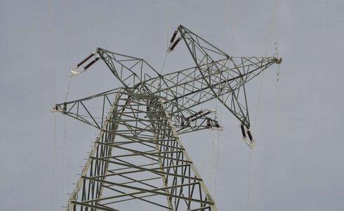 Hochspannungsmast mit einer sternenförmigen Struktur vor einem grauen Himmel.