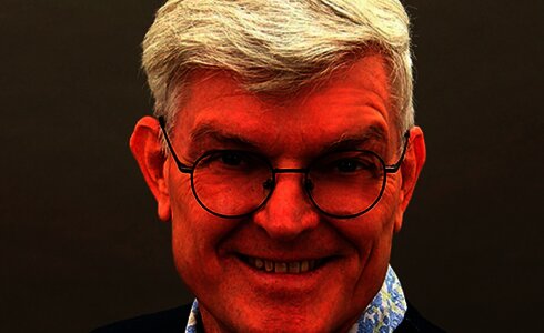 Ein lächelnder Mann mit kurzem, grauem Haar und Brille.