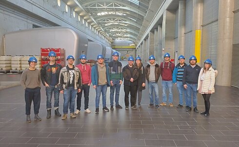Gruppe von 12 Personen mit blauen Helmen in einer modernen Industriehalle.