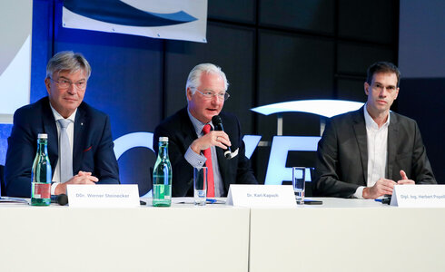 Drei Männer sitzen an einem Tisch und diskutieren während einer Konferenz.