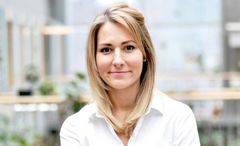 Junge Frau mit blonden Haaren, lächelt, steht mit verschränkten Armen.