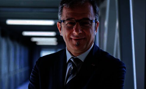 Ein lächelnder Mann in Anzug mit verschränkten Armen in einem modernen Gang.