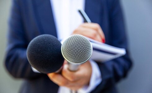 Eine Person hält zwei Mikrofone und macht sich Notizen auf einem Block.