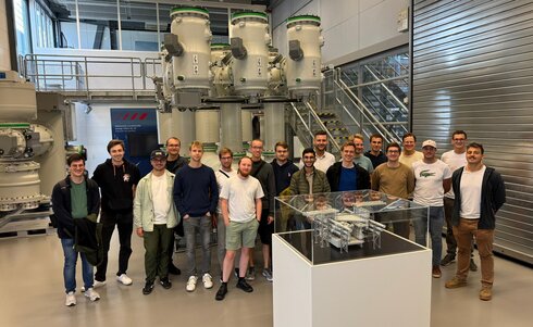 Gruppe von Personen steht vor industriellen Maschinen in einer modernen Fertigungshalle.