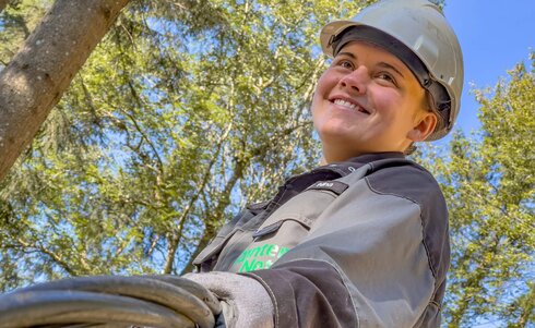 Eine lächelnde Person mit Helm, die Kabel in der Natur hält.