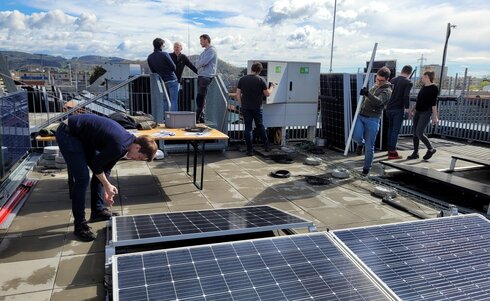 Menschen installieren Solarpanele auf einem Dach bei sonnigem Wetter.