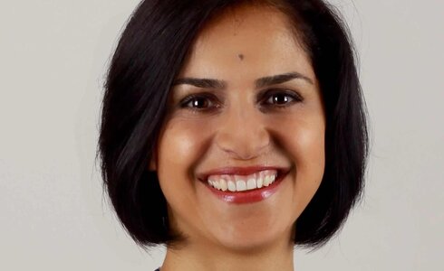 Eine lächelnde Frau mit schwarzem, schulterlangem Haar und einem eleganten Oberteil.