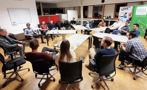 Eine Gruppe von Personen sitzt in einem Raum in einem Kreis und diskutiert.