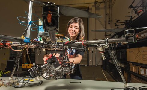 Eine junge Frau arbeitet an einer großen Drohne und lächelt dabei.
