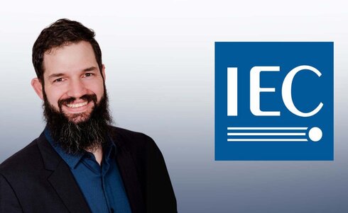 Mann mit Bart in Anzug neben dem IEC-Logo.