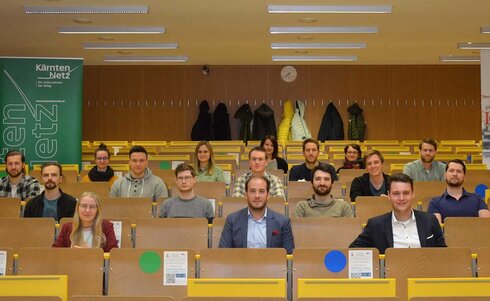 Gruppensitzung von Studierenden in einem Hörsaal mit Plakaten im Hintergrund.