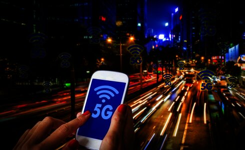 Eine Hand, die ein Smartphone mit 5G-Symbol in einer Stadt hält.