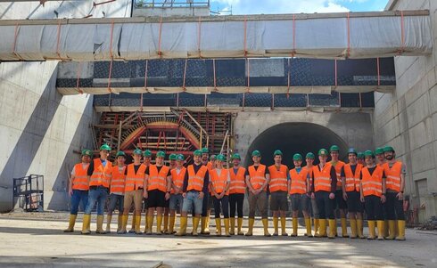 Gruppe von Bauarbeitern in Sicherheitswesten und Helmen vor einem Bauprojekt.