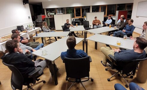 Gruppe von Menschen sitzt um Tische, diskutiert in einem hellen Raum.