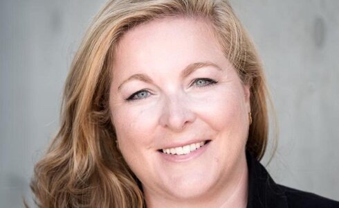 Porträt einer lächelnden Frau mit langen, blonden Haaren.