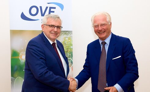 Zwei Männer schütteln sich die Hände vor einem OVF-Hintergrund.