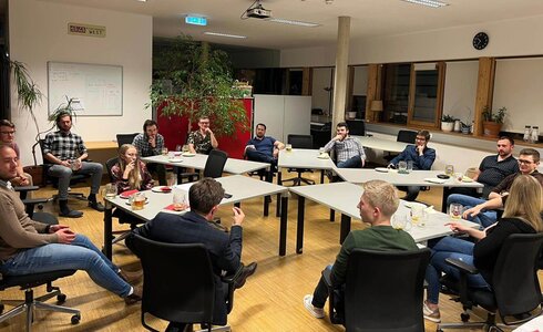 Eine Gruppe von Menschen sitzt entspannt in einem Raum um Konferenztische.