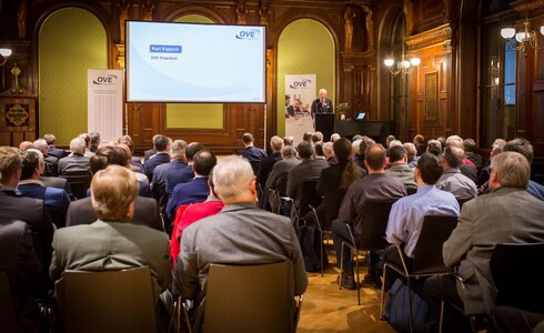Eine Person spricht vor einem Publikum in einem festlichen Saal.