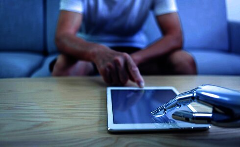 Eine menschliche Hand und eine Roboterhand berühren ein Tablet auf einem Tisch.