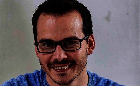 Ein lächelnder Mann mit Brille trägt einen blauen Pullover.