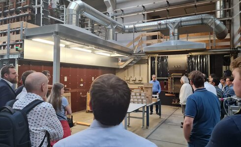 Gruppendiskussion in einem Labor mit einem Vortragender und technischen Geräten im Hintergrund.