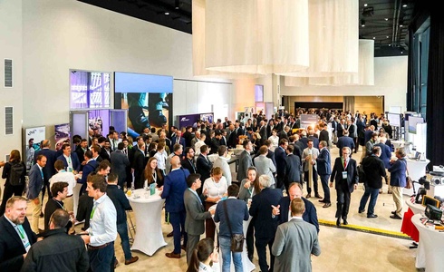 Menschenmenge auf einer Konferenz mit Stehtischen und Ausstellungsständen.