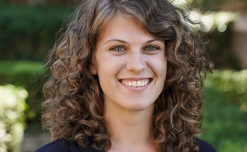 Eine lächelnde Frau mit lockigem Haar steht im Freien.