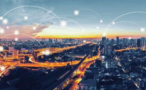 Städtische Skyline mit Verkehrswegen bei Sonnenuntergang und vernetztem Datenfluss.