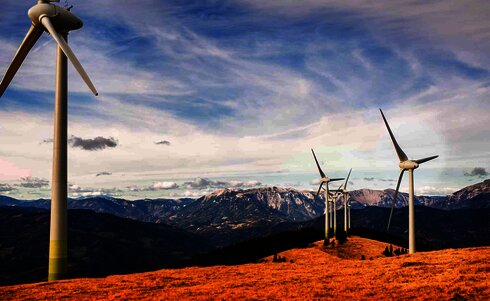 Windkraftanlagen stehen auf einem Hügel mit Bergen im Hintergrund.