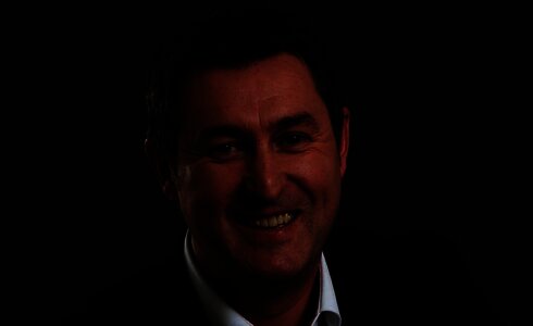 Lächelnder Mann in einem Anzug vor dunkelgrauem Hintergrund.