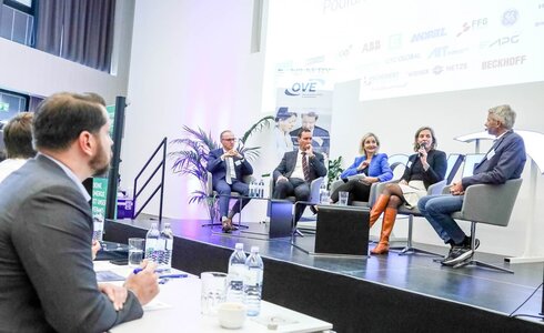 Podiumsdiskussion mit mehreren Sprechern und Publikum in einem modernen Veranstaltungsraum.