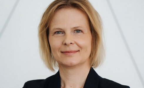 Porträt einer lächelnden Frau mit blonden Haaren und schwarzem Blazer.