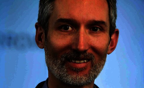 Porträt eines lächelnden Mannes mit grauem Bart und blonden Haaren.